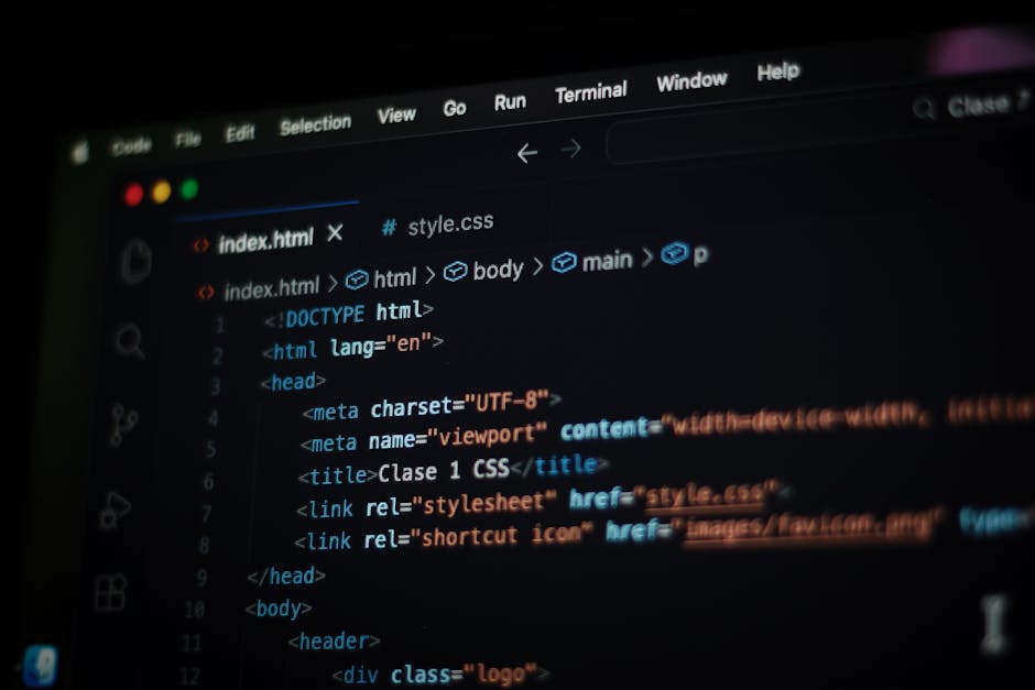 A close-up view of a person's right hand using a laptop with a silver keyboard on a wooden desk. The laptop screen displays lines of programming code with a black background and multicolored text. The